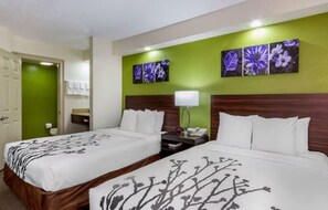 Une chambre d’hôtel avec deux lits, un mur d’accent de couleur verte et des œuvres d’art florales.