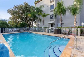 Une piscine dont la profondeur maximale est indiquée à 3 pieds et demi, entourée d’une clôture blanche, de palmiers et d’un bâtiment doté de balcons.