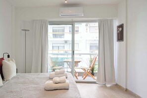 A hotel room with a bed, a bedside table, a lamp, a window with curtains, and a view of the outside balcony.