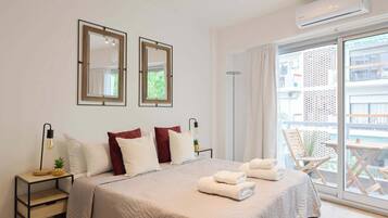 Habitación de hotel con una cama grande, dos mesitas de noche con lámparas, una ventana con vistas a edificios y un equipo de aire acondicionado.