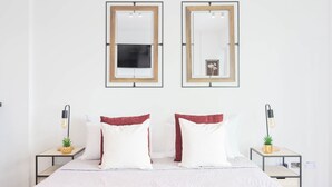 Un dormitorio ordenado con una cama, dos mesitas de noche, dos espejos colgados en la pared y una pequeña foto en marco.