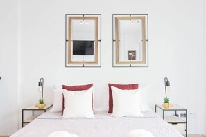 Una camera da letto ordinata con un letto, due comodini, due specchi fissati al muro e un piccolo quadro incorniciato.