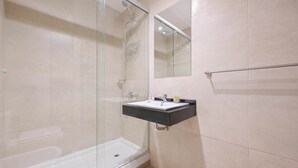Un baño moderno con ducha envuelta en vidrio, bañera blanca y lavamanos sobre encimera negra.