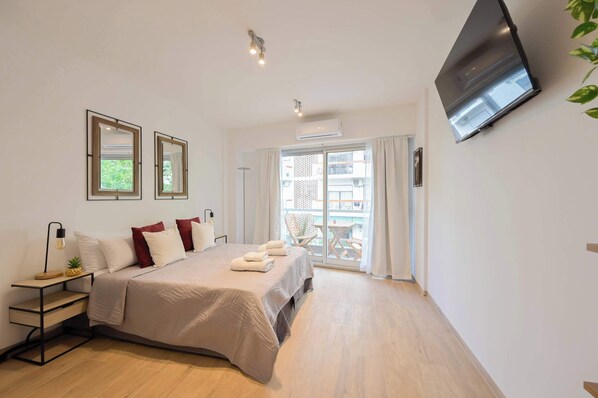 A modern hotel room with a bed, bedside table, lamp, air conditioning unit, and a TV mounted on the wall.
