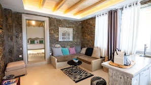 Un salon chaleureux avec un mur en pierre, un canapé avec des coussins, une petite table et un coin cuisine équipé d’un évier et d’un plan de travail.
