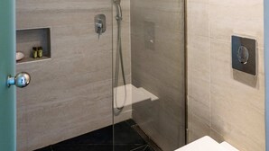 Une salle de bain moderne avec une douche à parois de verre, des toilettes et une petite étagère contenant des articles de toilette.