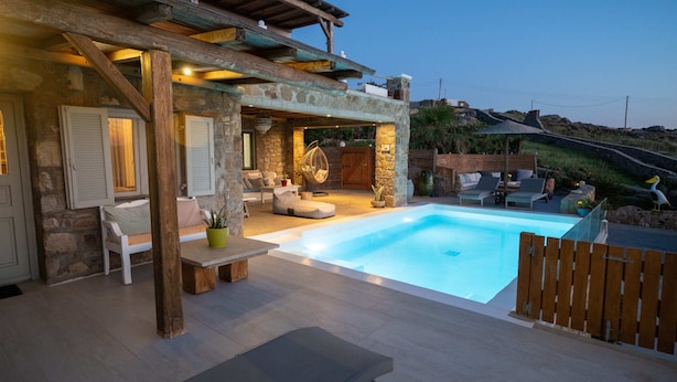 Un espace aménagé au bord de la piscine, avec des murs en pierre, des meubles en bois et un fauteuil suspendu.