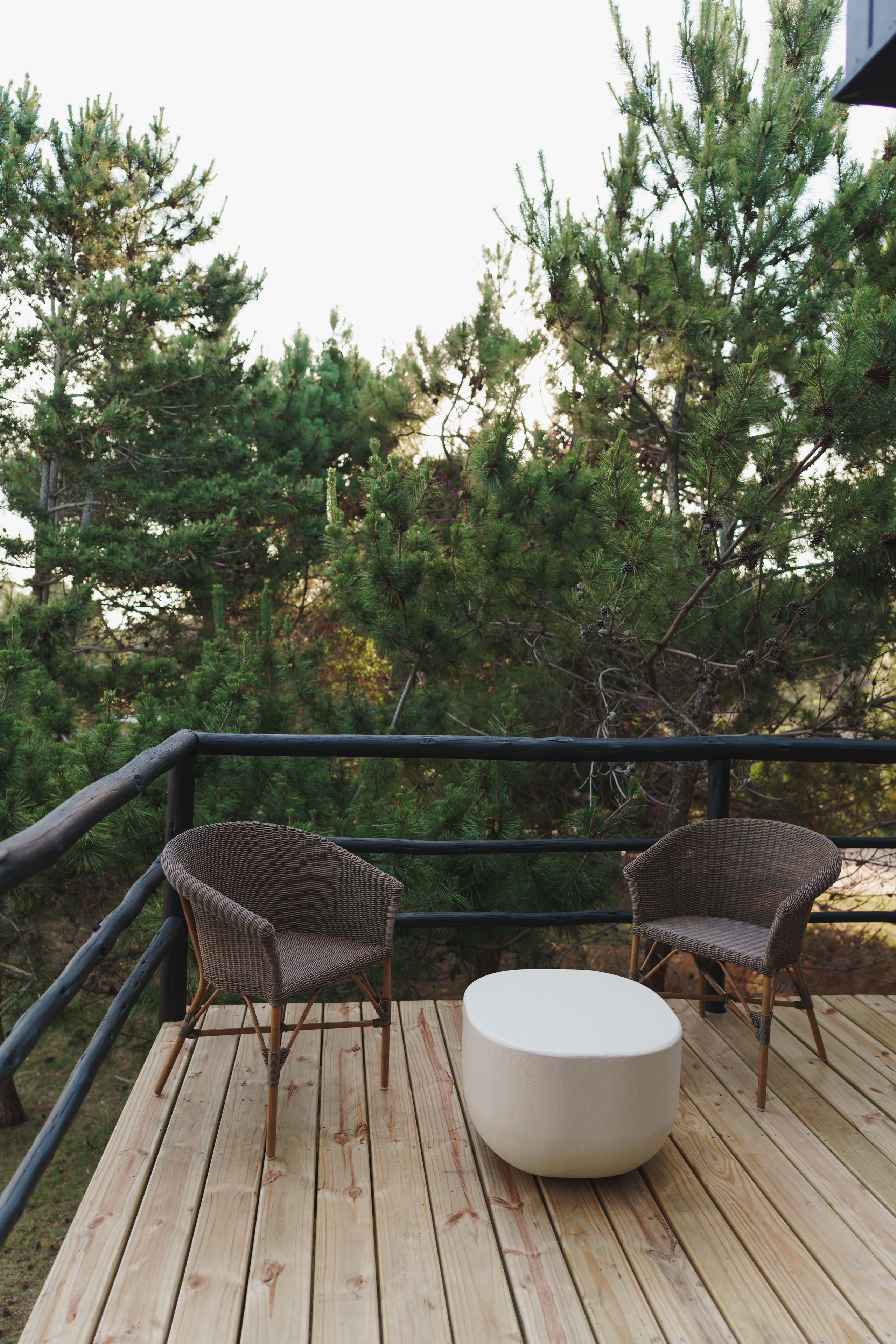 A wooden deck with two wicker chairs and a round table.