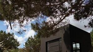 A modern building with a large garage door, surrounded by greenery and a concrete pathway leading to the entrance.