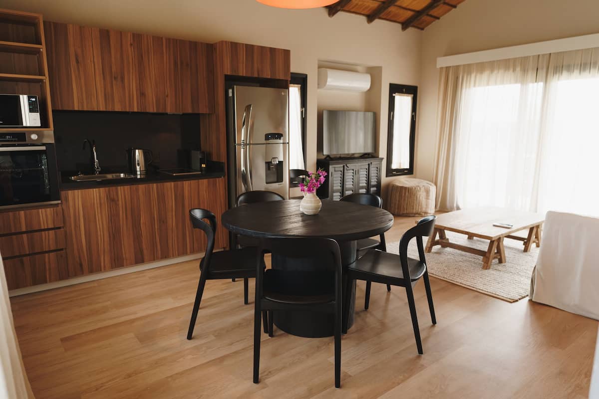A modern kitchen with wooden cabinets, a dining table with chairs, a refrigerator, and a television.