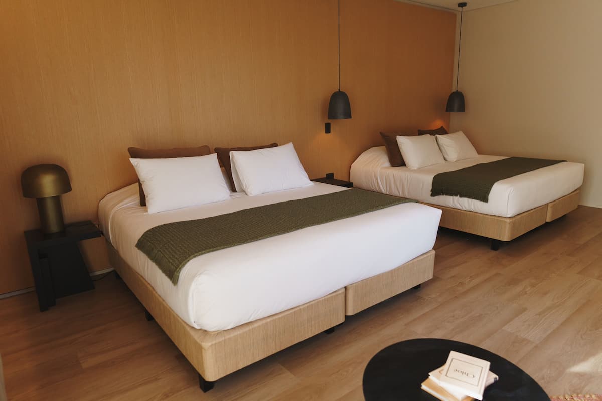 A hotel room with two beds, wooden flooring, and modern pendant lighting.