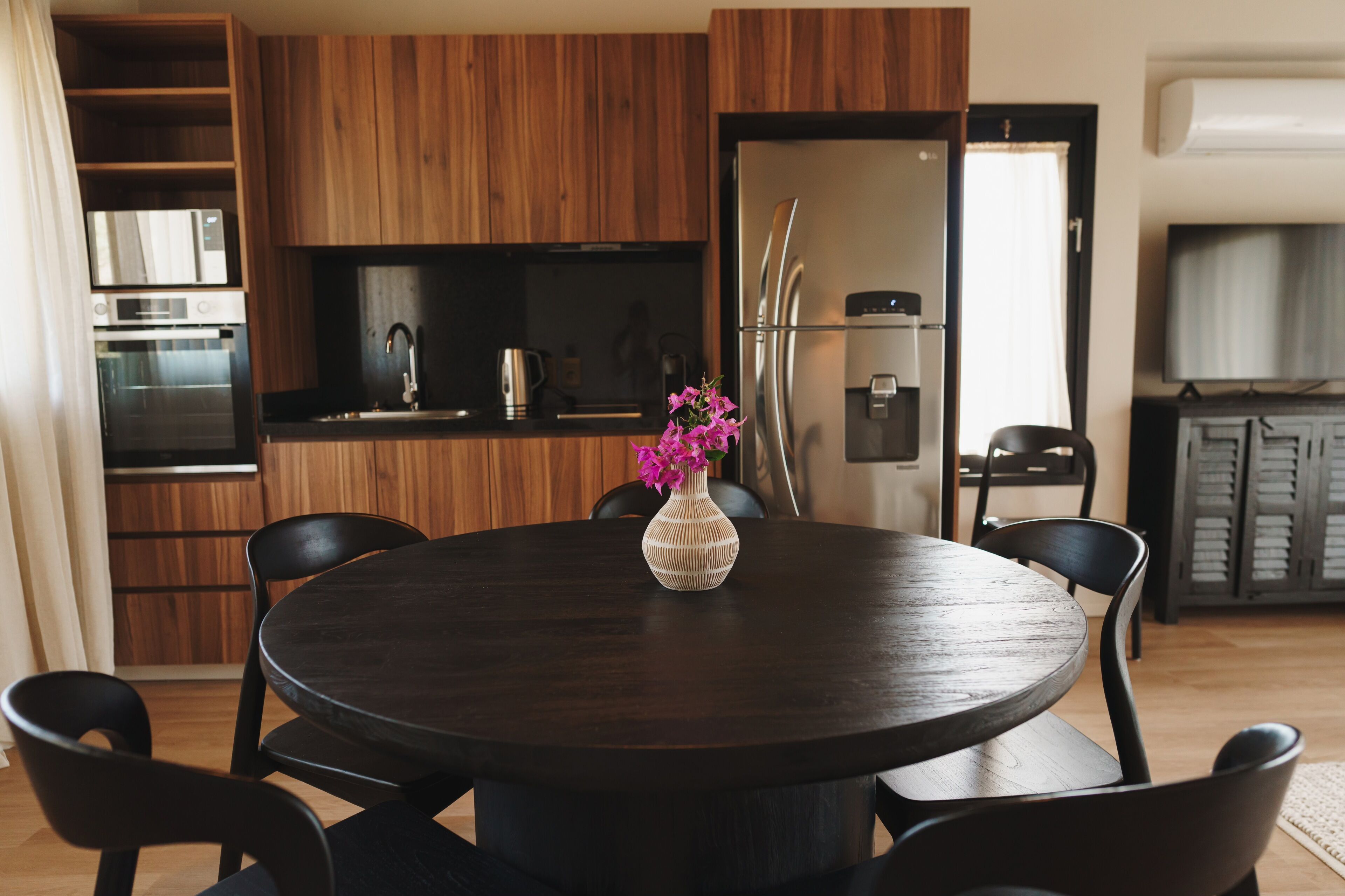 A modern kitchen with wooden cabinets, a stainless steel refrigerator, and a dining area with a round table and chairs.