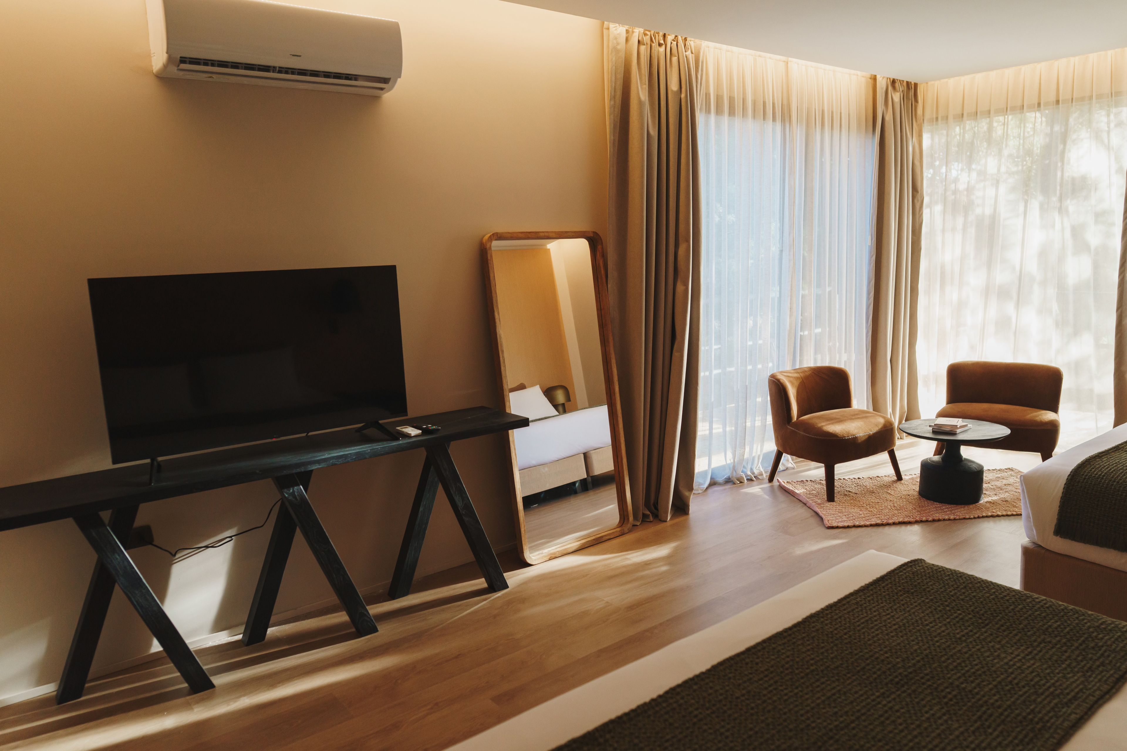 Ein Hotelzimmer mit Fernseher, einem Bett, einem Sessel, einem kleinen Tisch und einem Fenster mit Vorhängen.