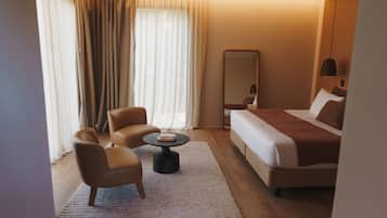 Habitación de hotel con cama, dos sillones, una mesita redonda, un espejo grande y una lámpara colgante.