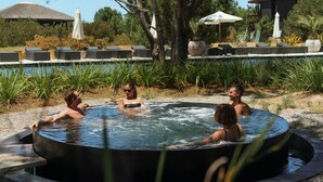 A hot tub area with lounge chairs and umbrellas, surrounded by trees and a pool.