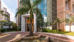 Un edifici modern amb façana de vidre reflectant, un pati ajardinat amb una palmera i una font.