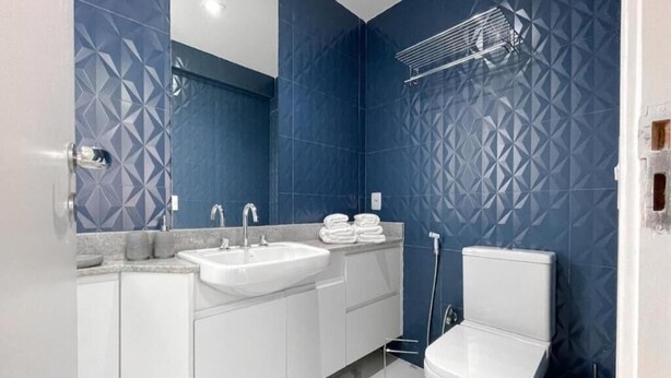 Un bany modern amb un lavabo blanc, un mirall i un vàter, amb parets de paper blau amb dibuixos.