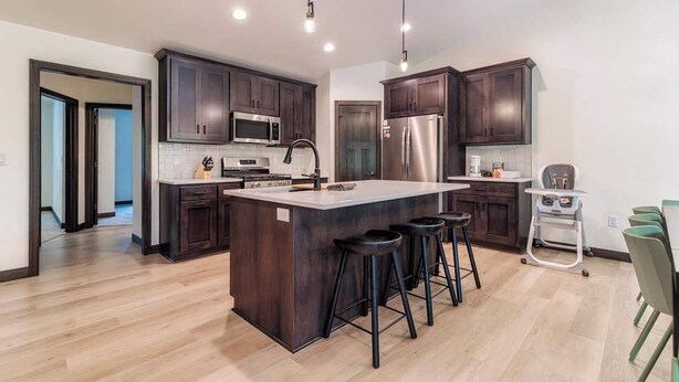 Una cocina moderna con armarios de madera oscura, electrodomésticos de acero inoxidable, una isla grande con taburetes e iluminación empotrada.