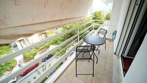 Een balkon met een tafel en stoelen, uitzicht op een straat met auto's en een groen gebied op de achtergrond.