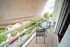 Ein Balkon mit Tisch und Stühlen, Blick auf eine Straße mit Autos und eine Grünfläche im Hintergrund.