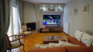 A living room with a flat-screen TV, wooden furniture, a fireplace, and framed artwork on the wall. - Poseidon Executive Suite in the heart of Athens Riviera. Edem beach and marina. (Paleo Faliro)
