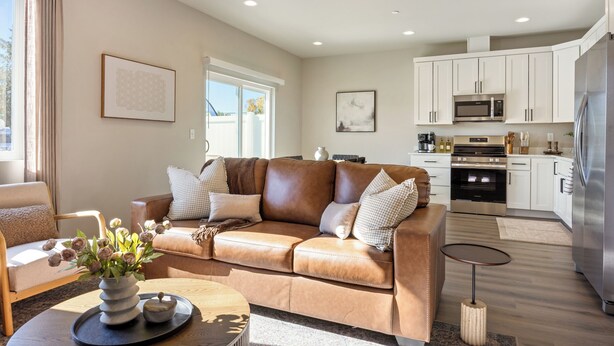 A modern living room with a leather sofa, a coffee table, and a kitchen area with white cabinets and stainless steel appliances. - NEW Ivy Streat Retreat in Ephrata, Sleeps 10, EV Charger + Foosball + Air Hockey (Ephrata)