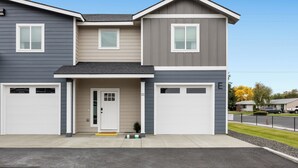 A two-story residential building with a garage on the ground floor, a front door, and a small porch area. - NEW Ivy Streat Retreat in Ephrata, Sleeps 10, EV Charger + Foosball + Air Hockey (Ephrata)
