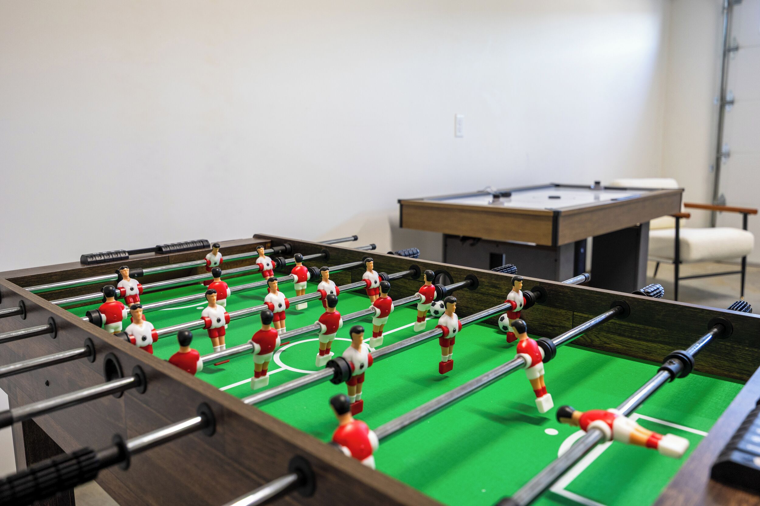 Une table de baby-foot avec des figurines rouges et blanches, dans une pièce où se trouvent également une table de billard et une chaise.