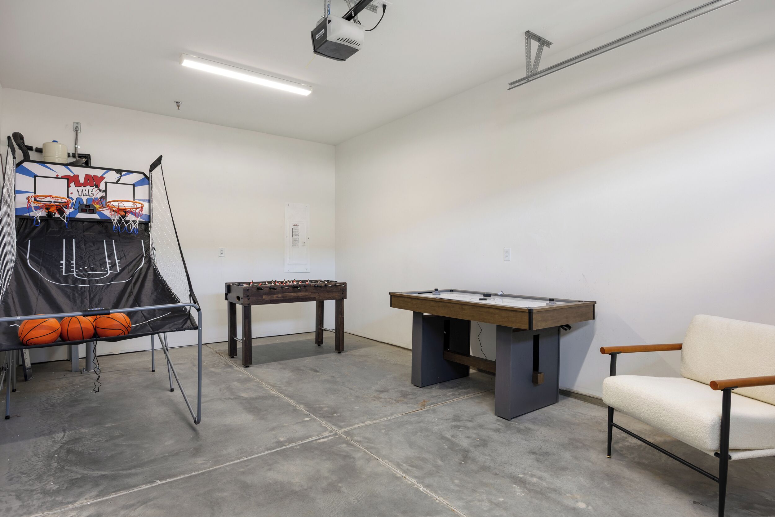 A room with a basketball hoop, foosball table, and a pool table.