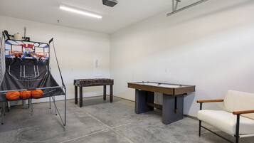 A room with a basketball hoop, foosball table, and a pool table.
