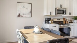 A modern kitchen with white cabinets, a stainless steel microwave, a coffee maker, and a large dining table with chairs. - NEW Ivy Streat Retreat in Ephrata, Sleeps 10, EV Charger + Foosball + Air Hockey (Ephrata)