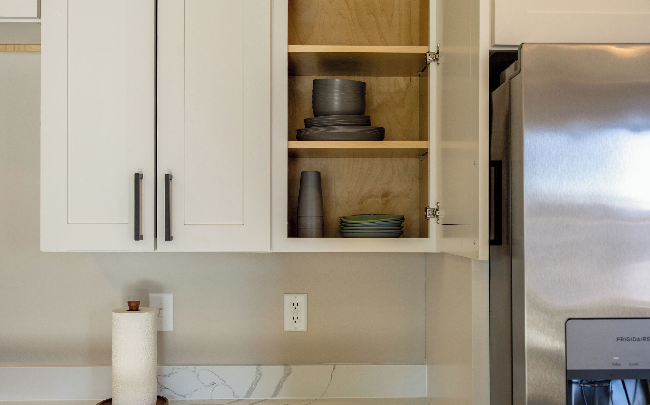 A kitchen with white cabinets, a stainless steel refrigerator, and a marble backsplash.