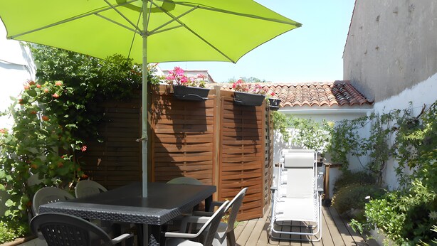 A patio with a table and chairs, a green umbrella, and a white chair. - Holiday Home "La Maison des Ormeaux" with Private Terrace and Wi-Fi (Ars-en-Ré)