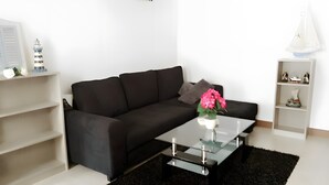 A modern living room with a black sofa, a glass coffee table, and a white shelf with decorative items. - Holiday Home "La Maison des Ormeaux" with Private Terrace and Wi-Fi (Ars-en-Ré)