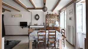 A dining area with a table set for six, a television, a clock, and a shelf with dishes. - Holiday Home "La Maison des Ormeaux" with Private Terrace and Wi-Fi (Ars-en-Ré)