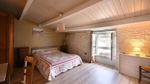 A bedroom with a bed, wooden floor, a window, a lamp, and a door. - Holiday Home "La Maison des Ormeaux" with Private Terrace and Wi-Fi (Ars-en-Ré)