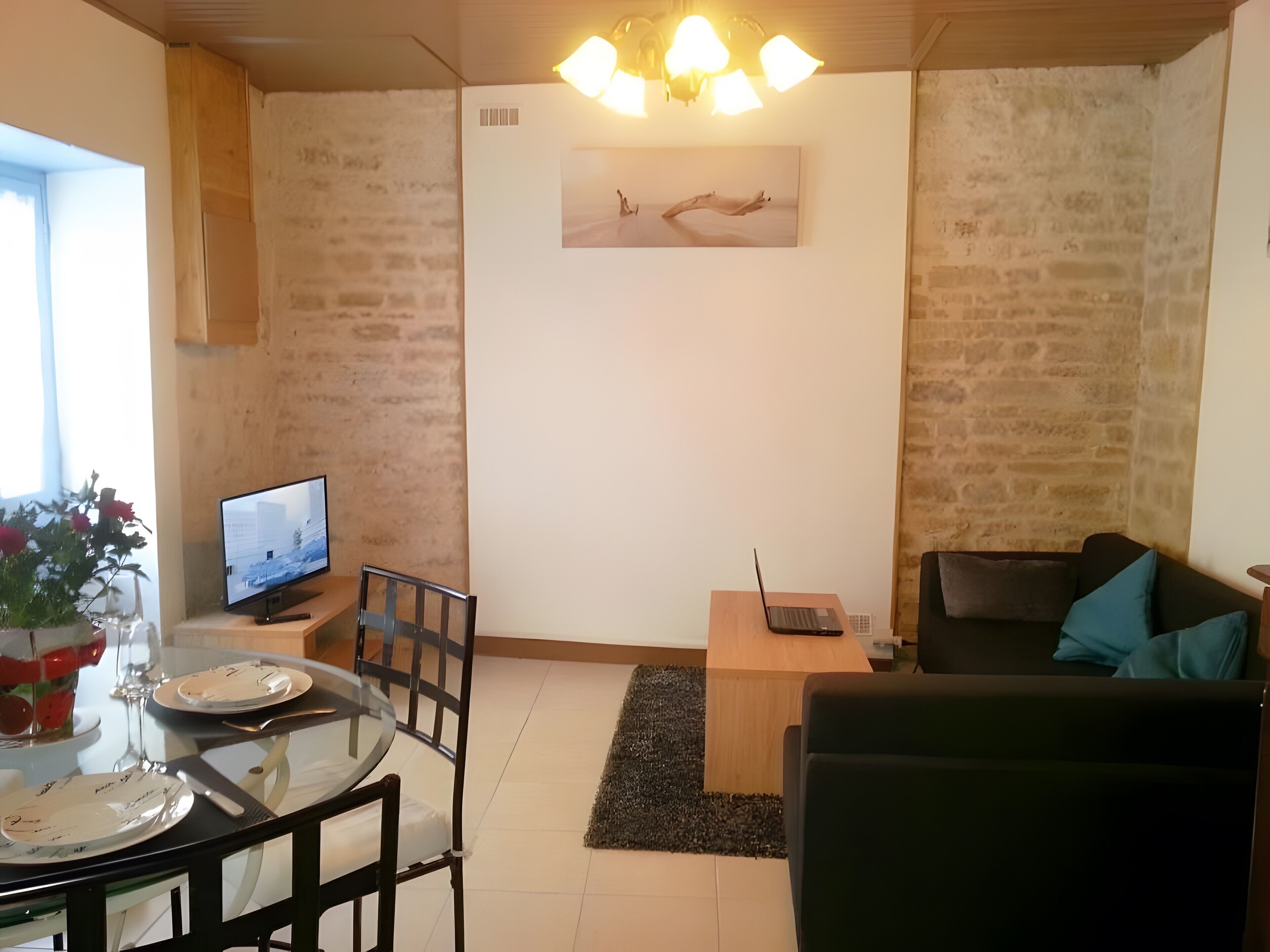 En stue med et fjernsyn, en bærbar computer, en sofa og et spiseområde med et bord og stole.