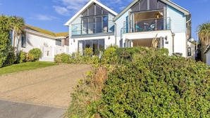 A modern two-story house with large windows, a covered driveway, and lush greenery. - Spring Tide, 3 bedrooms, Sea views, Bigbury on Sea (Bigbury on Sea, Kingsbridge)