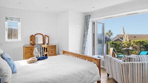 A bedroom with a large bed, a wooden dresser, a mirror, and a view of the outside. - Spring Tide, 3 bedrooms, Sea views, Bigbury on Sea (Bigbury on Sea, Kingsbridge)