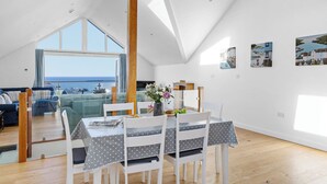 A spacious room with a high ceiling, a dining area with a table and chairs, and a large window offering a view of the sea. - Spring Tide, 3 bedrooms, Sea views, Bigbury on Sea (Bigbury on Sea, Kingsbridge)