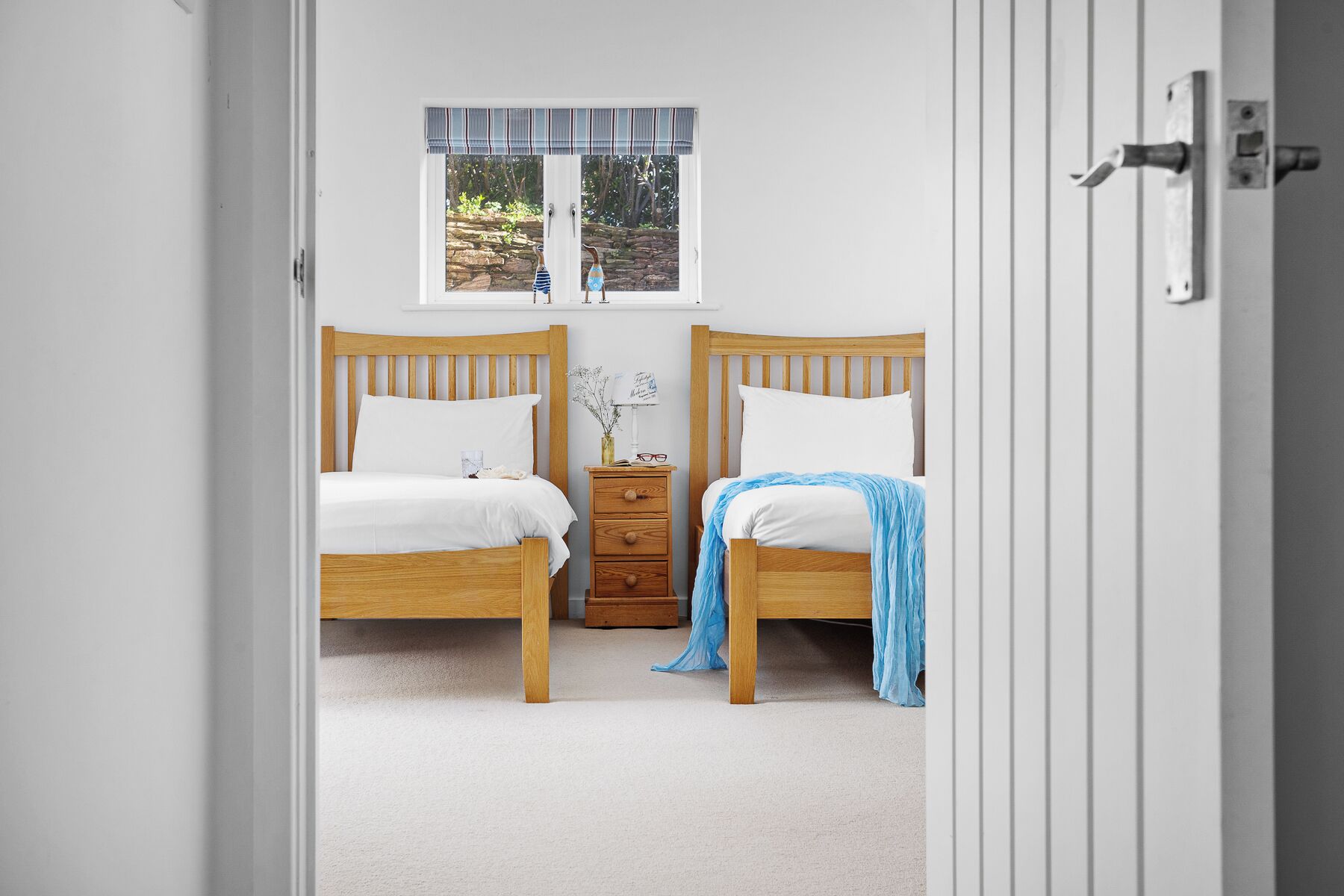 A bedroom with two wooden beds, a nightstand, and a window with a view of greenery.