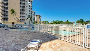A pool area with lounge chairs, a pool, and a building with multiple balconies in the background. - Walk to Bonita Beach: Top-floor Condo w/ Views (Bonita Springs)