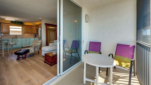 Un balcon avec une porte-fenêtre coulissante, une petite table et deux chaises colorées.