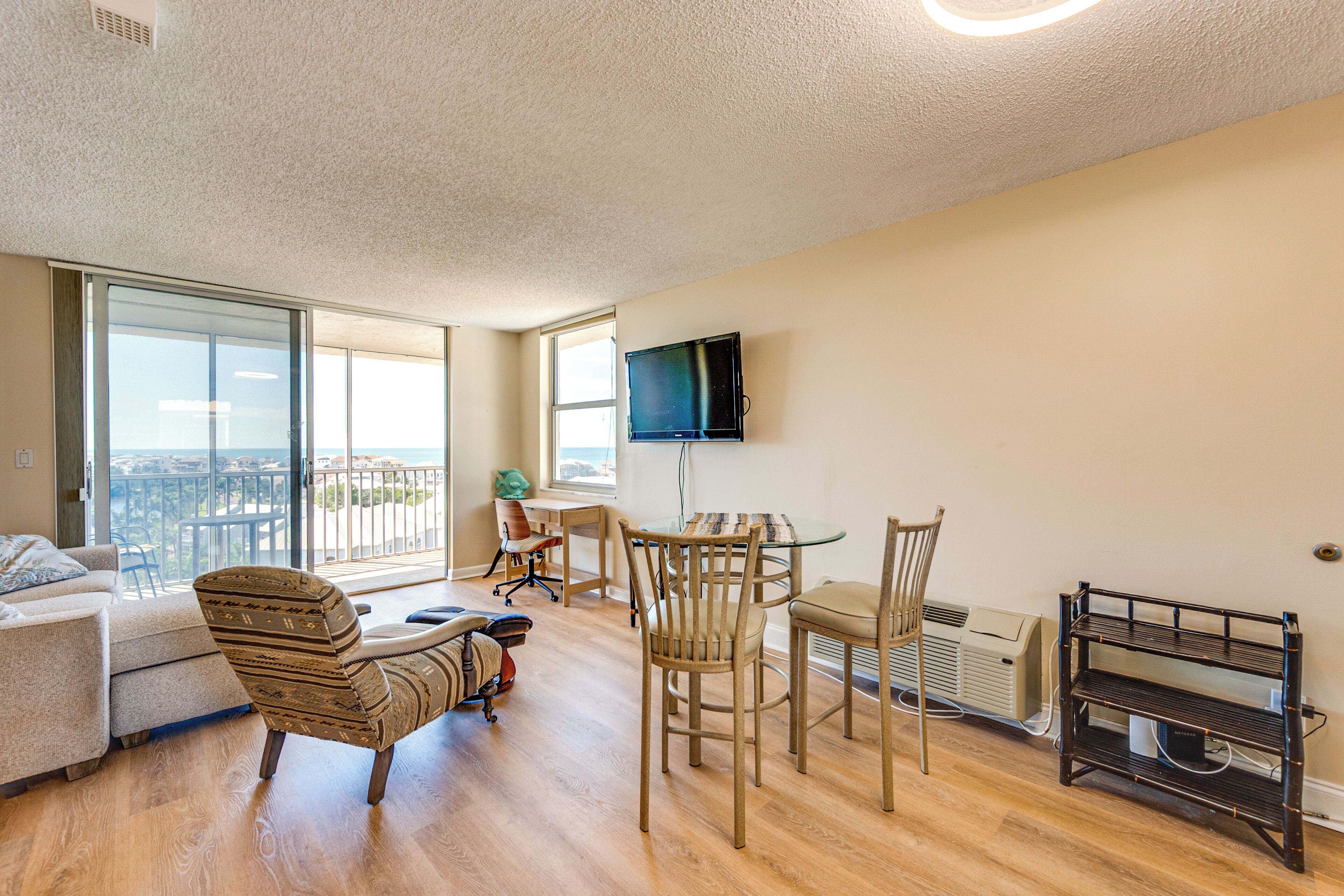 A spacious living room with a balcony, a dining area, and a TV mounted on the wall.