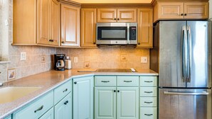 A kitchen with light green cabinets, a stainless steel refrigerator, and a built-in microwave. - Walk to Bonita Beach: Top-floor Condo w/ Views (Bonita Springs)