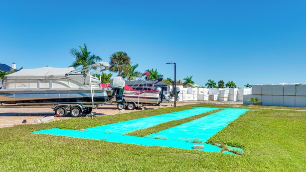 A grassy area with a blue mat, a trailer, and a boat with a canopy. - Walk to Bonita Beach: Top-floor Condo w/ Views (Bonita Springs)