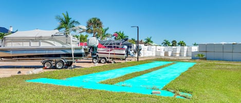 Une zone herbeuse avec un tapis bleu, une remorque et un bateau doté d’un auvent.