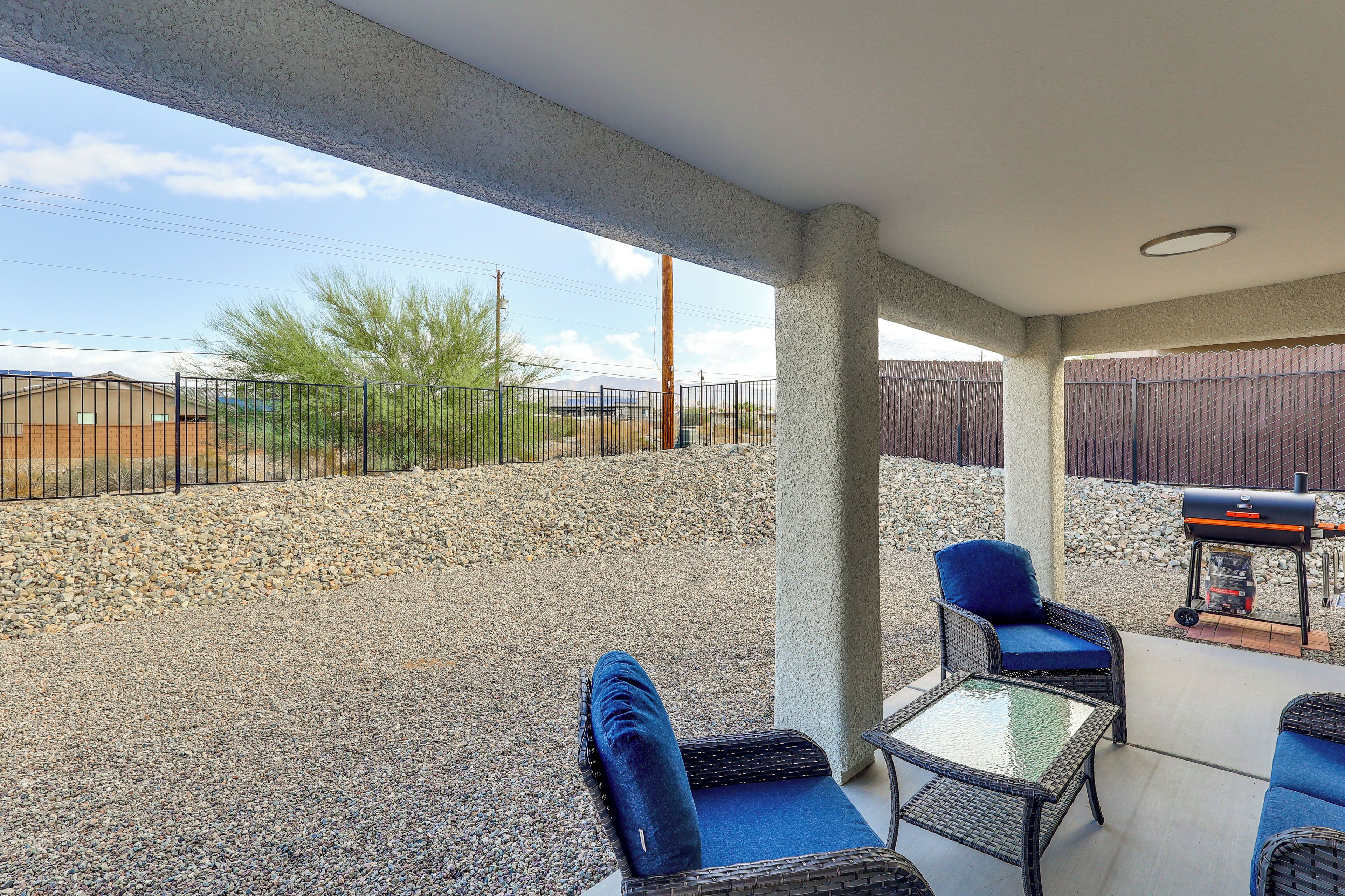 An outdoor patio with wicker furniture, a grill, and a view of a fenced area with a mountain in the background.