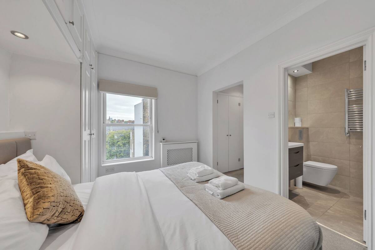 A modern hotel room with a bed, a window, a bathroom, and a view of the city.
