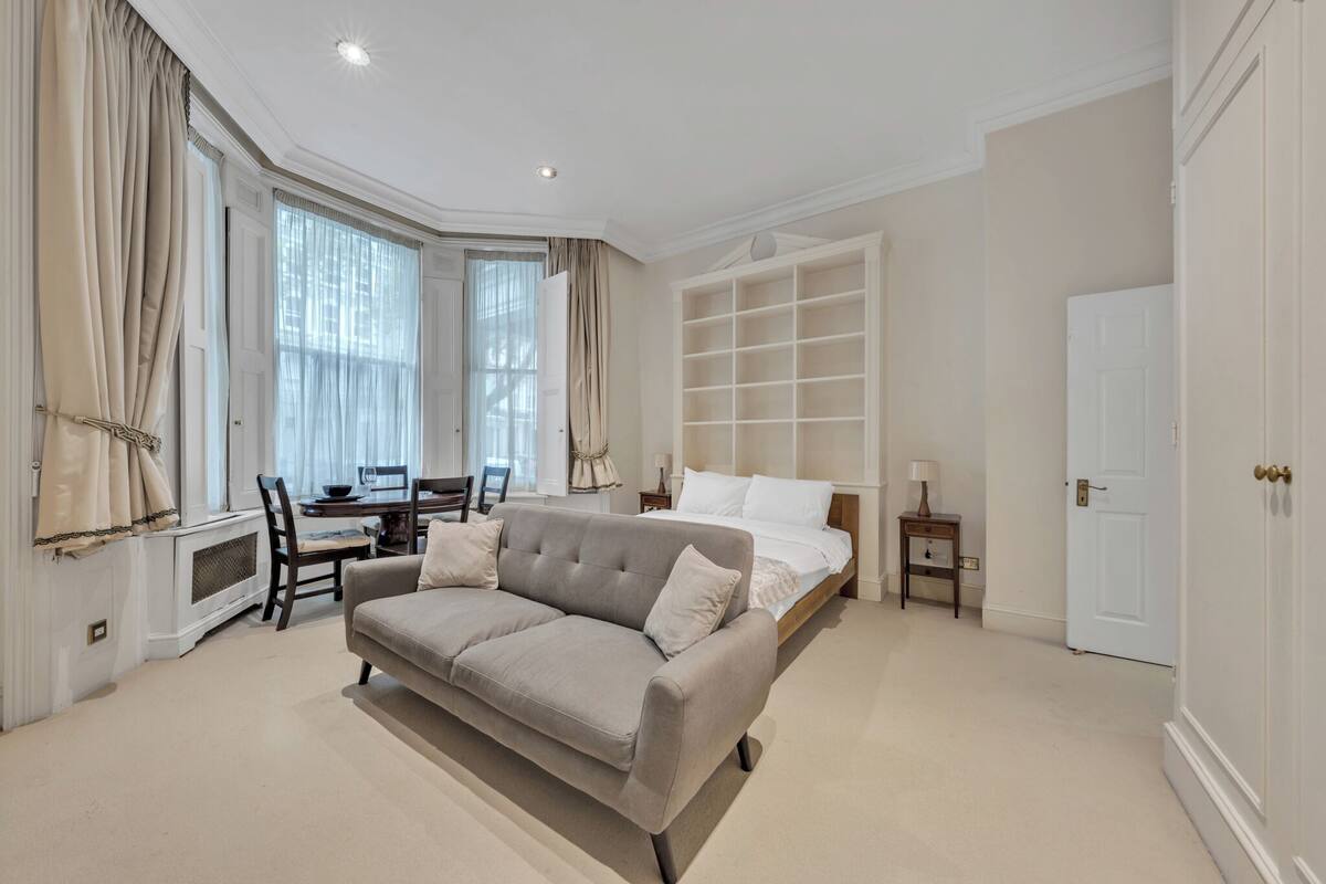 A spacious bedroom with a large bed, a sofa, a desk, and a built-in bookshelf.